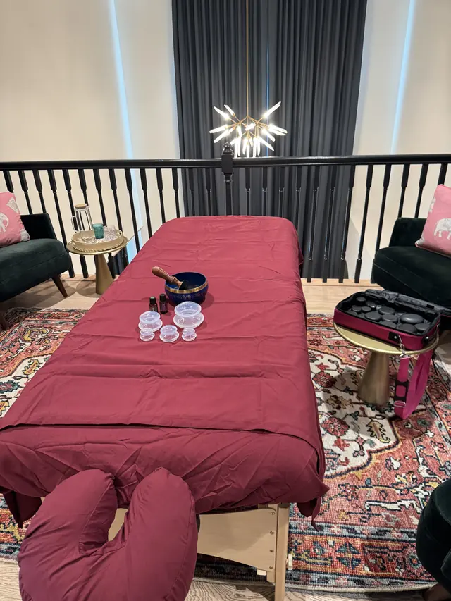 The Light Awakener mobile massage setup: professional table with fresh linens, hot stones, cupping set and oils, arranged in a client's home